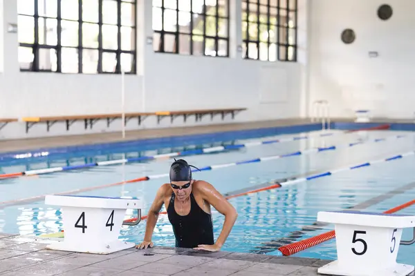 白人女性アスリートは屋内施設でプールから登ります 彼女は厳しい泳ぎの後に強さと決意を示す水泳選手です — ストック写真