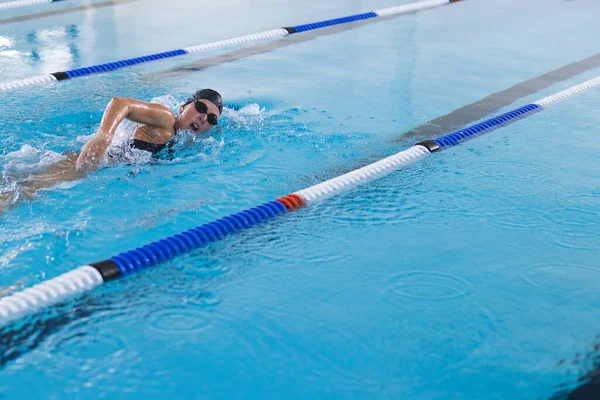 Caucasian female athlete swimmer swimming in a pool. She is practicing her freestyle stroke in an indoor swimming facility.