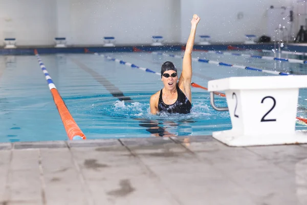 Caucasian female athlete swimmer celebrates a swim victory at the pool.  Her raised fist signifies triumph in a competitive swimming event.