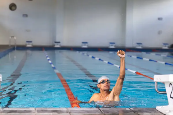 A swimmer reaches the end of the pool in an indoor facility.  The athlete\'s determination is evident in this competitive swimming environment.
