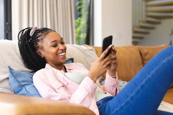 Genç Afrikalı Amerikalı Kadın Akıllı Telefonunu Kullanırken Gülümsüyor Kanepede Rahatça — Stok fotoğraf