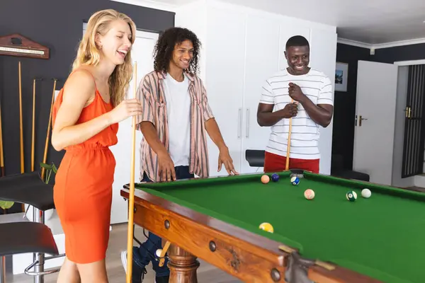 身穿红色衣服的年轻白人女人和一个白人男人和一个非裔美国男人一起玩游泳池 他们在随意的室内环境中享受着游戏 享受着片刻的闲暇和乐趣 — 图库照片