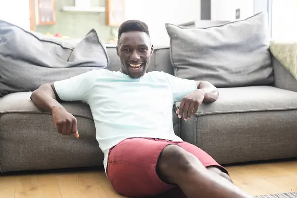 Ein Junger Afroamerikaner Lümmelt Auf Einem Grauen Sofa Und Lächelt — Stockfoto