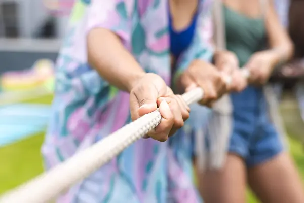 Close-up of hands gripping a rope in a tug-of-war competition, focus on teamwork and effort. Participants wear casual clothing, highlighting a fun and competitive outdoor activity.