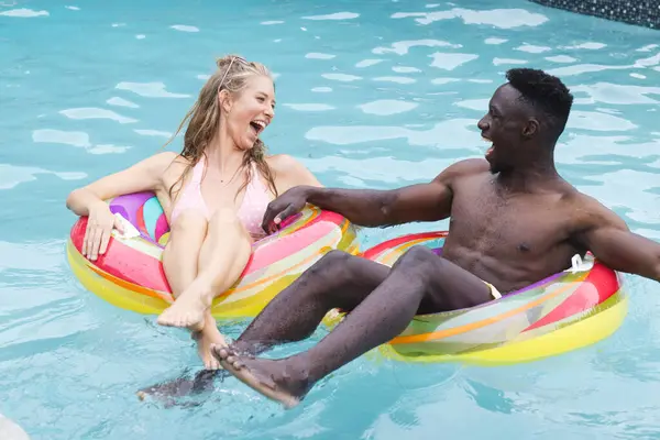 年轻的白人女人和非裔美国男人在五彩缤纷的游泳池上一起欢笑 他们在游泳池里享受着欢乐的时刻 这意味着休闲和放松 图库图片