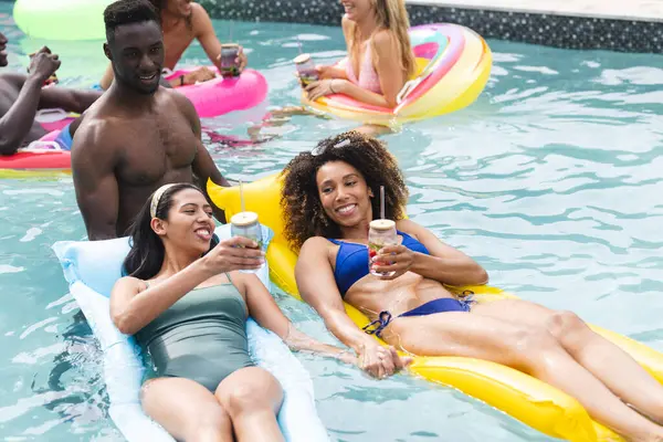 若いアフリカ系アメリカ人男性と女性はプールパーティーを楽しむ 彼らはカラフルなインフレータブルに囲まれた飲み物で浮遊しています ストック写真
