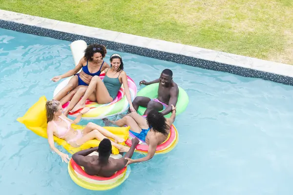 五花八门的朋友们在五彩缤纷的花坛上享受着一个泳池派对 在阳光明媚的室外环境中 年轻的非裔美国男女们一起欢笑 免版税图库照片