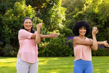 Mature biracial woman and young biracial woman exercising in garden at home. Both wearing casual clothes, mature woman with dark hair, young with curly hair, unaltered clipart