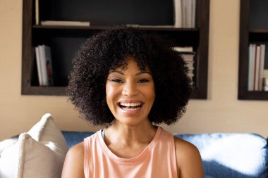 Young biracial woman with curly black hair smiling at home. She wears simple tank top and has a joyful expression, unaltered clipart