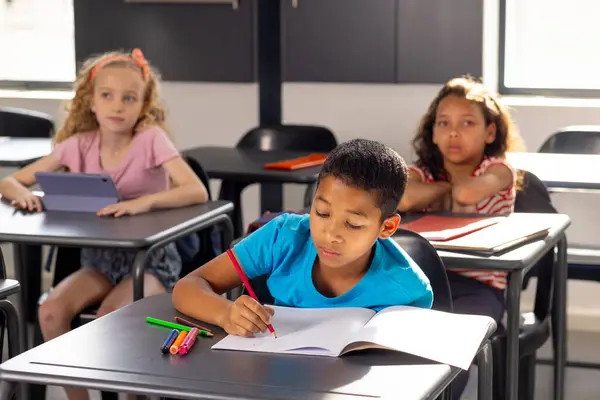 School Classroom Boy Blue Shirt Writing Notebook Two Girls Watching — Stock Photo, Image