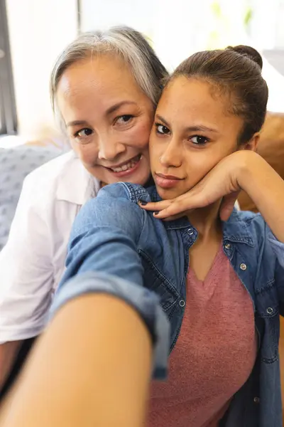 Asian Grandmother Embracing Biracial Teenage Granddaughter Home Both Smiling Camera Stock Image