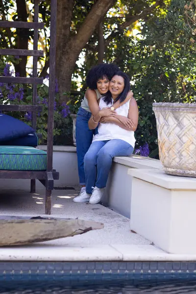赤ん坊の母親と大人の娘は庭の自宅の庭のベンチに抱擁しています 両方とも暗い髪を持っています カールと若い カジュアルな服を着る 変更されていない ロイヤリティフリーのストック写真