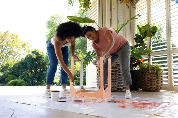 Biracial Mãe Filha Adulta Estão Pintando Uma Cadeira Rosa Fora Fotos De Bancos De Imagens