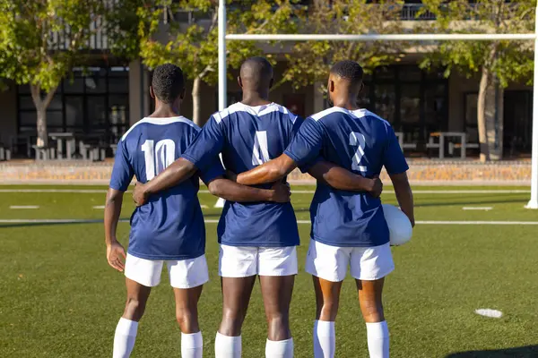 Three African American Young Male Athletes Hug Rugby Field Outdoors Stock Photo