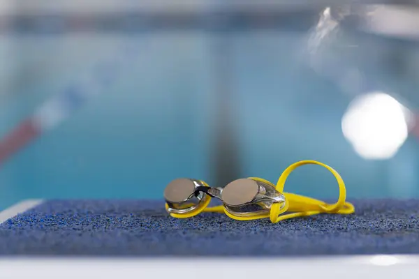屋内プールの端 明確な水反射光 コピースペースで休むゴーグル ゴーグルに焦点を当てることは 変更されていない水泳の準備を示唆しています ストック画像