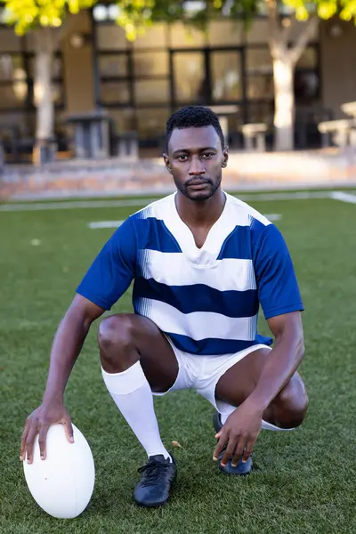 Afrikansk Amerikansk Ung Mannlig Idrettsutøver Kneler Banen Utendørs Holder Rugbyball stockfoto