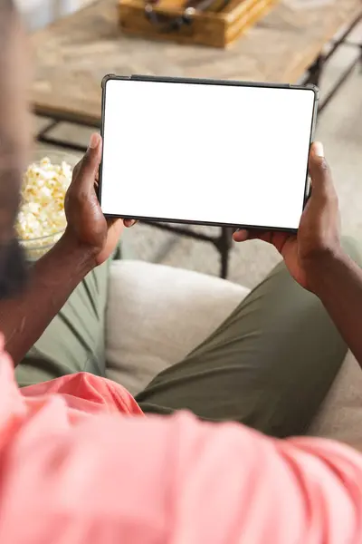 非洲裔美国人在家里很放松 拿着空白的平板屏幕和复制空间 他穿着休闲装 黑发短发 坐在沙发上 一动不动 免版税图库照片