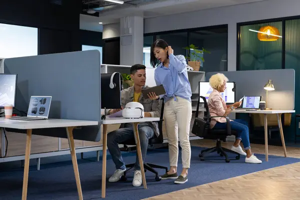 stock image A diverse group of Business colleagues collaborates in a modern office, one showing a tablet. The office features open workspaces, computers, and a collaborative atmosphere, unaltered