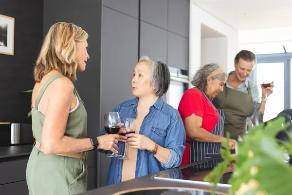 stock image Diverse group of mature women enjoying wine and conversation in modern kitchen. Retirement, friendship, senior living, happiness, unaltered