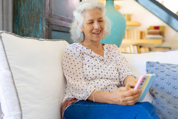 Senior woman smiling and using smartphone while relaxing on couch at home. Technology, elderly, lifestyle, relaxation, communication, unaltered — Stock Image Senior Woman Smiling Using Smartphone While Relaxing Couch Home Technology Royalty Free Stock Images