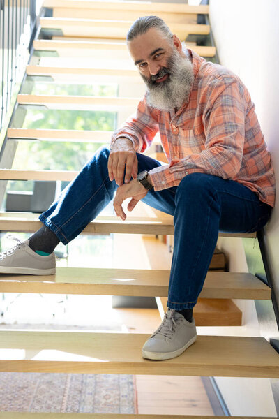 At home, Smiling senior man sitting on stairs, wearing casual clothes, looking relaxed. relaxing, lifestyle, older adult, staircase, unaltered — Stock Image Home Smiling Senior Man Sitting Stairs Wearing Casual Clothes Looking Stock Picture