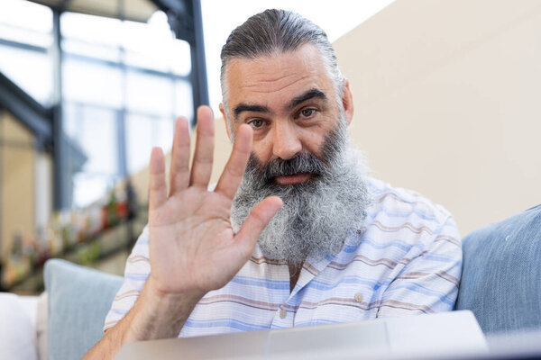 Senior man waving hand while video chatting on laptop at home. Technology, communication, elderly, video call, online, connection, unaltered — Stock Image Senior Man Waving Hand While Video Chatting Laptop Home Technology Stock Photo