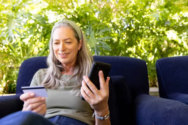 stock image Shopping online, mature woman holding smartphone and credit card, sitting on couch. E-commerce, online shopping, mobile payment, digital purchase, home, convenience