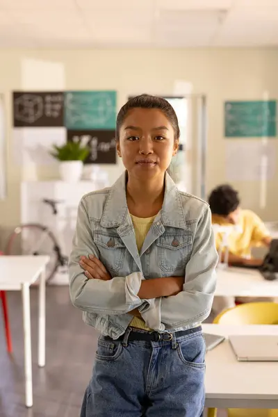 stock image Teenage girl in high school classroom standing with arms crossed, looking confident. Student, confidence, education, learning, empowerment, youth