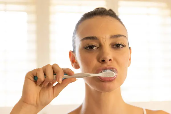 stock image Brushing teeth, young woman focusing on dental hygiene in bathroom. Dental care, oral hygiene, toothpaste, toothbrush, clean, health