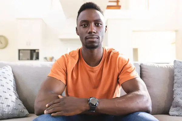 stock image Serious african american man having video call, sitting on sofa at home listening. Communication, technology, domestic life and lifestyle, unaltered.