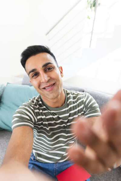 Middle Eastern man reaching out to the camera during a video call from a cozy home setting. His friendly gesture adds a personal touch to the inviting atmosphere. — Stock Image Middle Eastern Man Reaching Out Camera Video Call Cozy Home Royalty Free Stock Photos