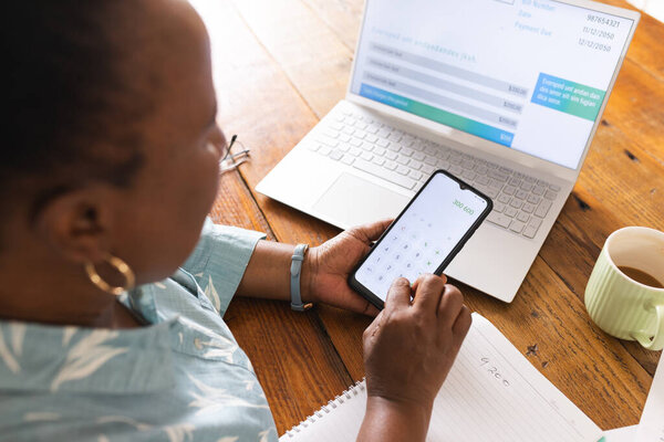Busy senior african american woman with documents on table calculating on smartphone at home. Domestic life, retirement, technology and lifestyle, unaltered. — Stock Image Busy Senior African American Woman Documents Table Calculating Smartphone Home Royalty Free Stock Photos