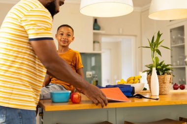 Packing school bag, father and son preparing for school in kitchen. Parenting, family, morning routine, preparation, bonding, childhood, back to school  clipart