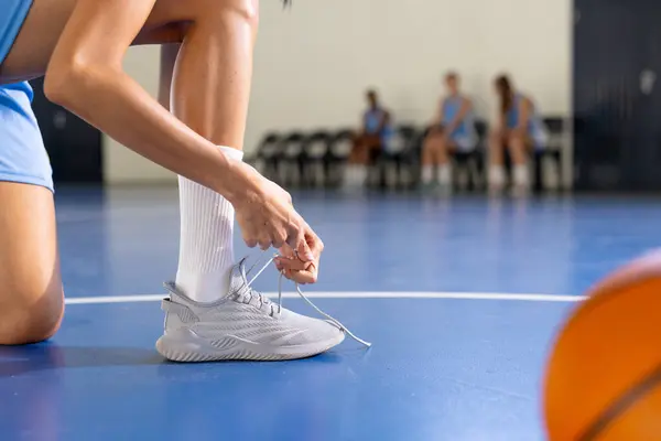 Tying shoelaces, female basketball player preparing for game on court, copy space. Sport, preparation, athlete, footwear, competition, active