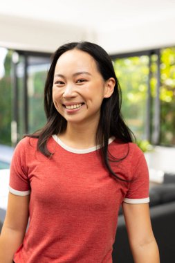 Smiling young asian woman in casual red shirt standing indoors, looking at camera. Portrait, cheerful, confident clipart