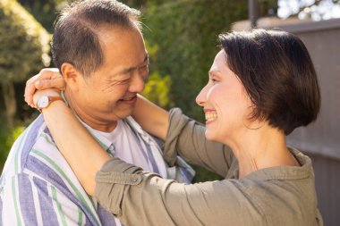 Smiling multiracial middle-aged couple embracing outdoors, enjoying quality time together in garden. Romance, happiness, togetherness, nature, affection, bonding clipart