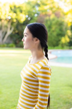 Young asian woman with braided hair standing outdoors in striped shirt, looking thoughtful. casual, fashion, hairstyle, contemplation, summer, female clipart