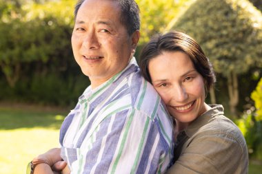 Smiling multiracial middle-aged couple embracing outdoors, enjoying quality time together in garden. Love, romance, togetherness, nature, happiness, relationship clipart