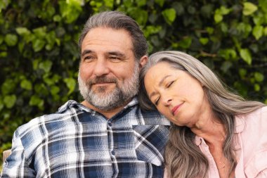 Relaxing outdoors, mature couple smiling as woman rests head on man's shoulder. relationship, happiness, bond, connection, tranquility, leisure clipart