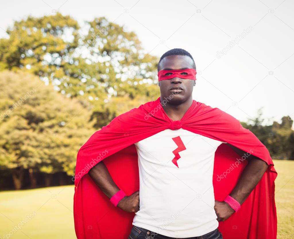 African American man standing in park wearing red cape and superhero mask with lightning-bolt logo. Cosplay, costume, heroism, empowerment, confidence, roleplay, action