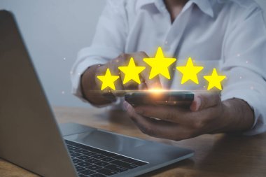 İş adamı iyi derecelendirme, dijital pazarlama, iyi deneyim, müşteri değerlendirmesi, müşteri geribildirim kavramını gözden geçirmek için beş yıldızlı cep telefonu ve laptop kullanıyor.