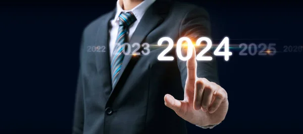 Goal. businessman hand touching and pointing on year 2024 with virtual screen on dark background, goal target, change from 2023 to 2024, strategy, investment, business planning, happy new year concept