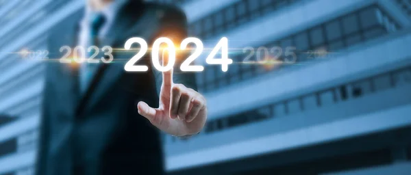 2024. business man hand pointing on year 2024 with virtual screen on building background, goal target, change from 2023 to 2024, strategy, investment, business planning, happy new year concept