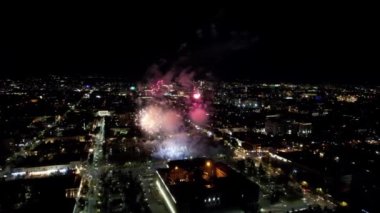 Şehir merkezindeki havai fişeklerden gelen büyük parlak ışıklar. Gece şehri Almaty 'deki bir İHA' nın hava görüntüsü, renkli ışıklar ve fenerler. İnsanlar dinleniyor. Arabalar geliyor. Şehirde bir tatil.