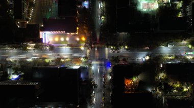 Gece kavşağındaki bir dronun kuş bakışı görüntüsü. Yol boyunca küçük bir araba ve otobüs akıntısı hareket ediyor. Yol boyunca fenerler ve evlerden gelen ışıklar parlıyor. Bir sürü ağaç.