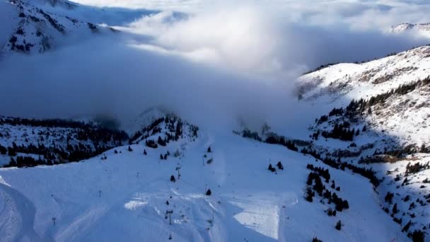 从空中俯瞰雪山和白云 贡多拉路 有小木屋人们正在滑雪板上滑行 针叶树生长 一片云雾弥漫在峡谷中 — 图库视频影像