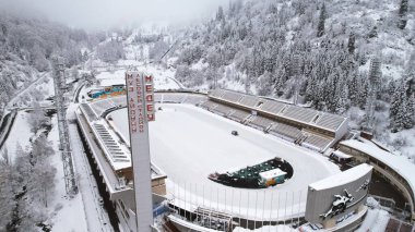 Dağlarda kış Alp Paten Pisti Medeo. Karlı ormanın ve dağların drone görüntüsü. Beyaz bulutlar ve sis vadide. Kar temizleme işlemi başladı. Büyük bir stadyum. Almaty, Kazakistan