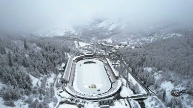 Dağlarda kış Alp Paten Pisti Medeo. Karlı ormanın ve dağların drone görüntüsü. Beyaz bulutlar ve sis vadide. Kar temizleme işlemi başladı. Büyük bir stadyum. Almaty, Kazakistan