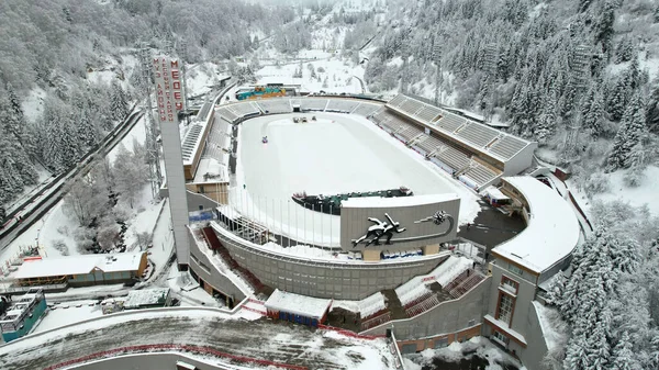 Dağlarda kış Alp Paten Pisti Medeo. Karlı ormanın ve dağların drone görüntüsü. Beyaz bulutlar ve sis vadide. Kar temizleme işlemi başladı. Büyük bir stadyum. Almaty, Kazakistan