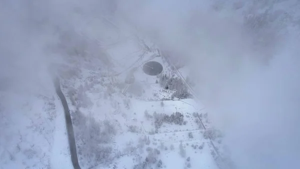 stock image Snowy mountains with coniferous trees in the clouds. Medeo Dam. Everything is in fog and snow. Christmas and New Year have come. Aerial view from the drone on road, dam and trees. Almaty, Kazakhstan